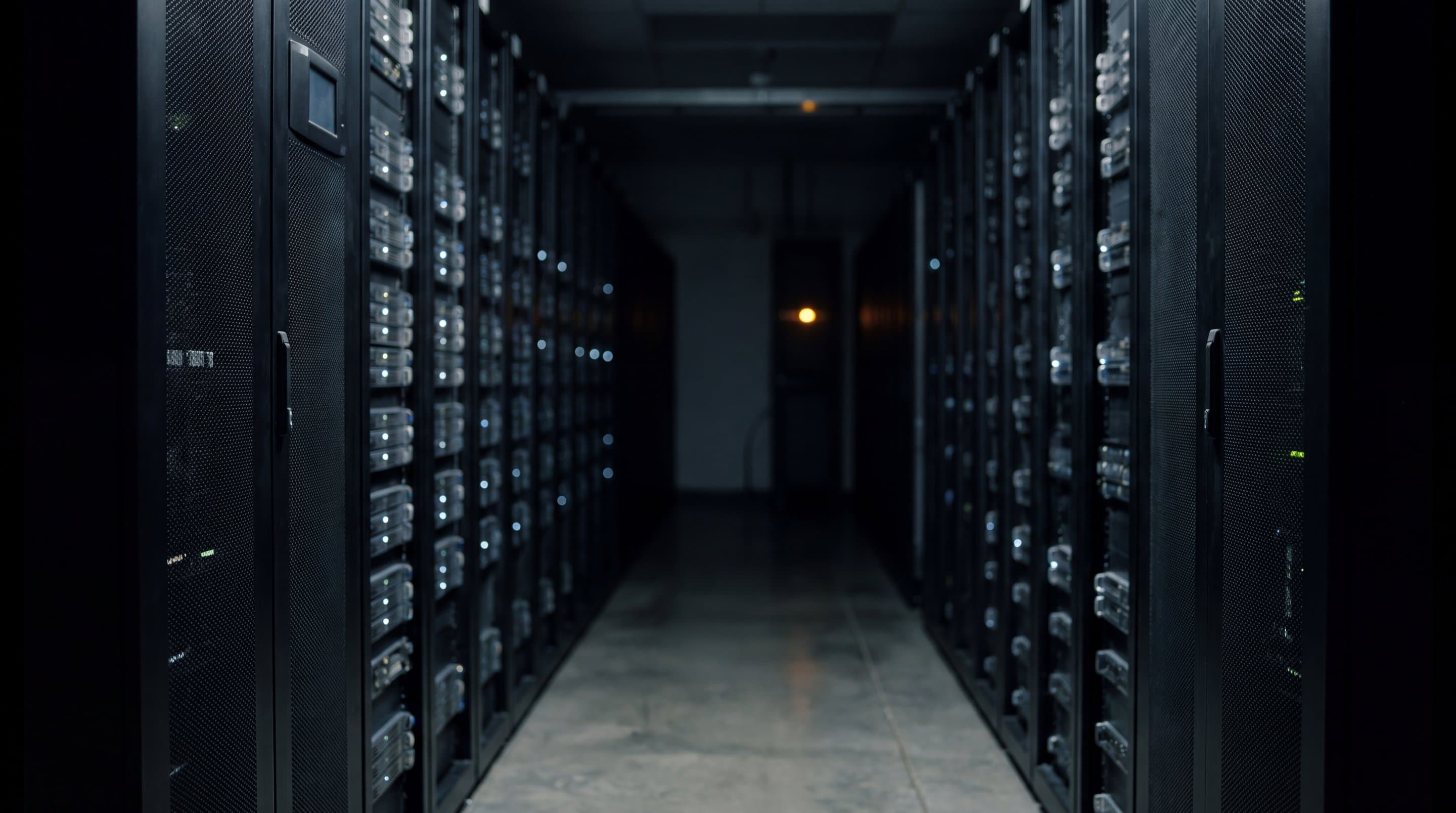 A hospital server room at night, racks receding into the dark, one warm light far down the aisle.