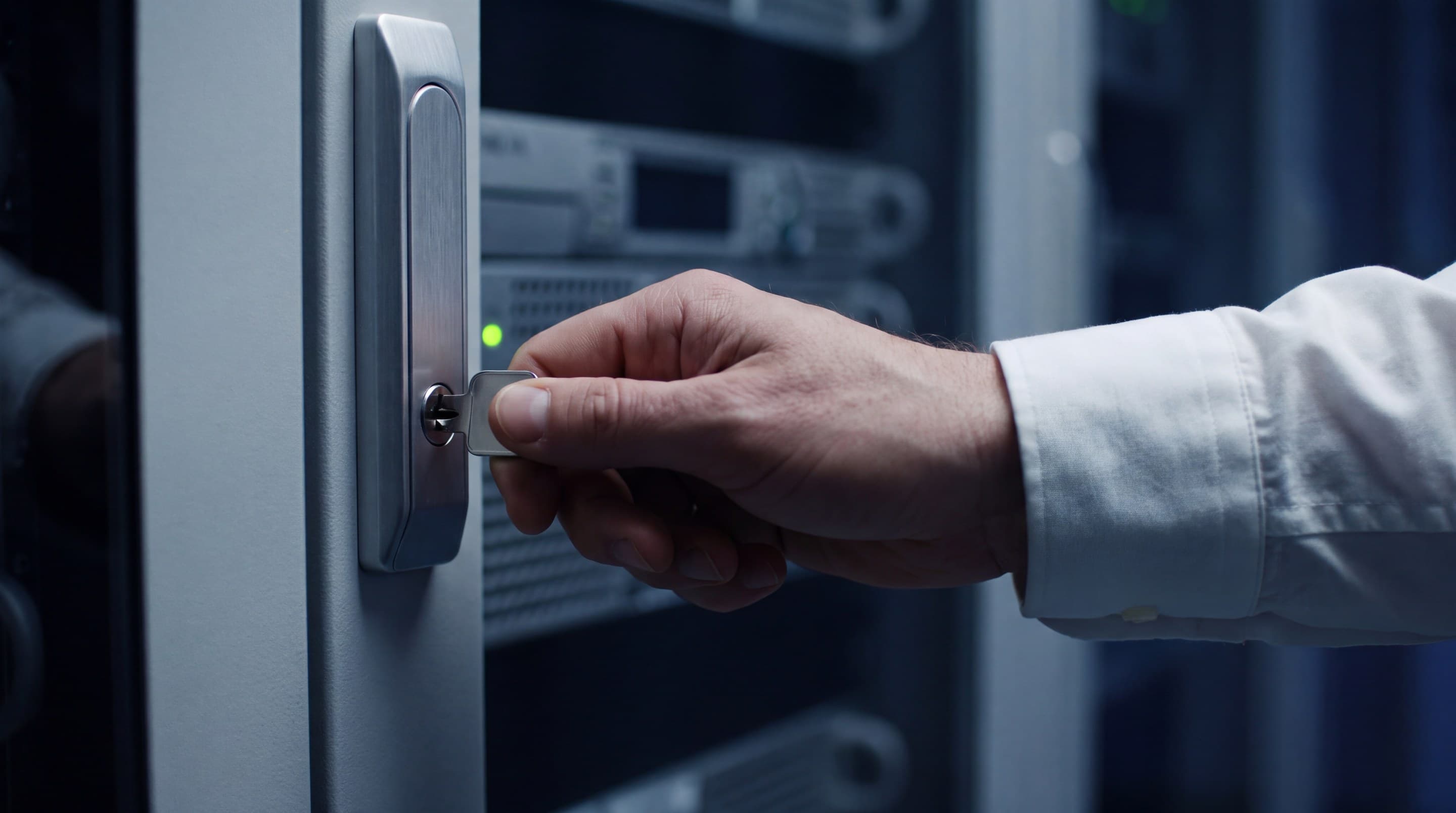 A hand turning a key in a server cabinet lock, a green status light beside it.